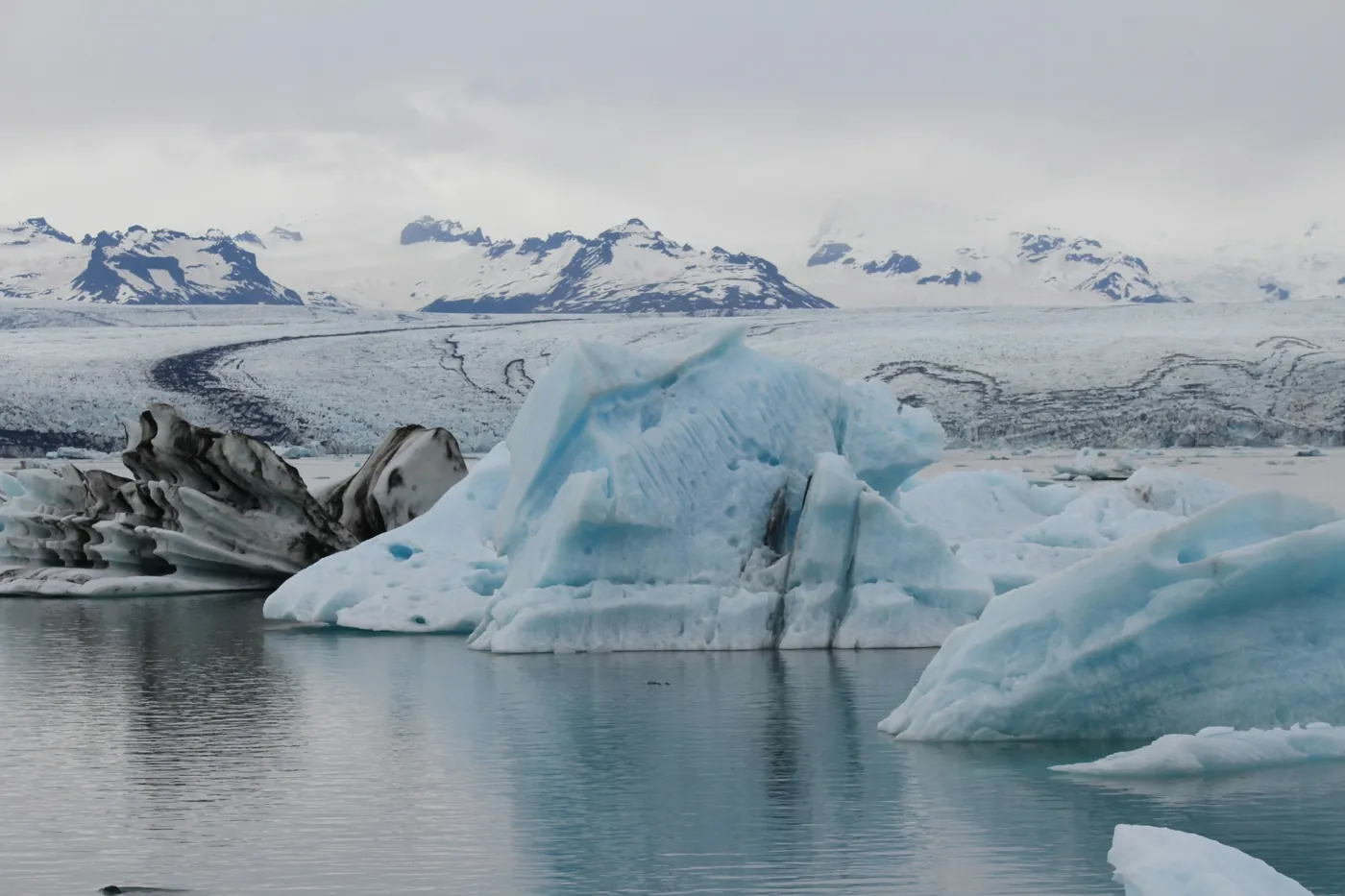 Eisberge in der Gletscherlagune Jökulsárlón bei Tag, dahinter der Gletscher und Berge
