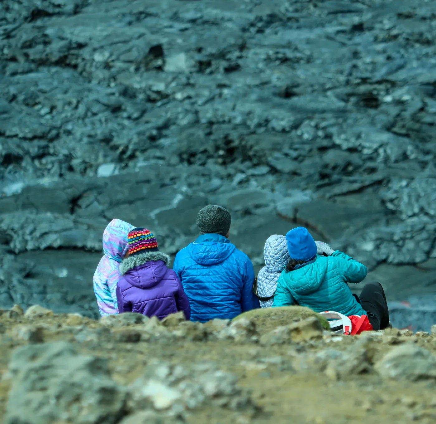 Familie mit Kindern in Winterjacken sitzt am Rand eines erkalteten Lavafelds am Fagradalsfjall
