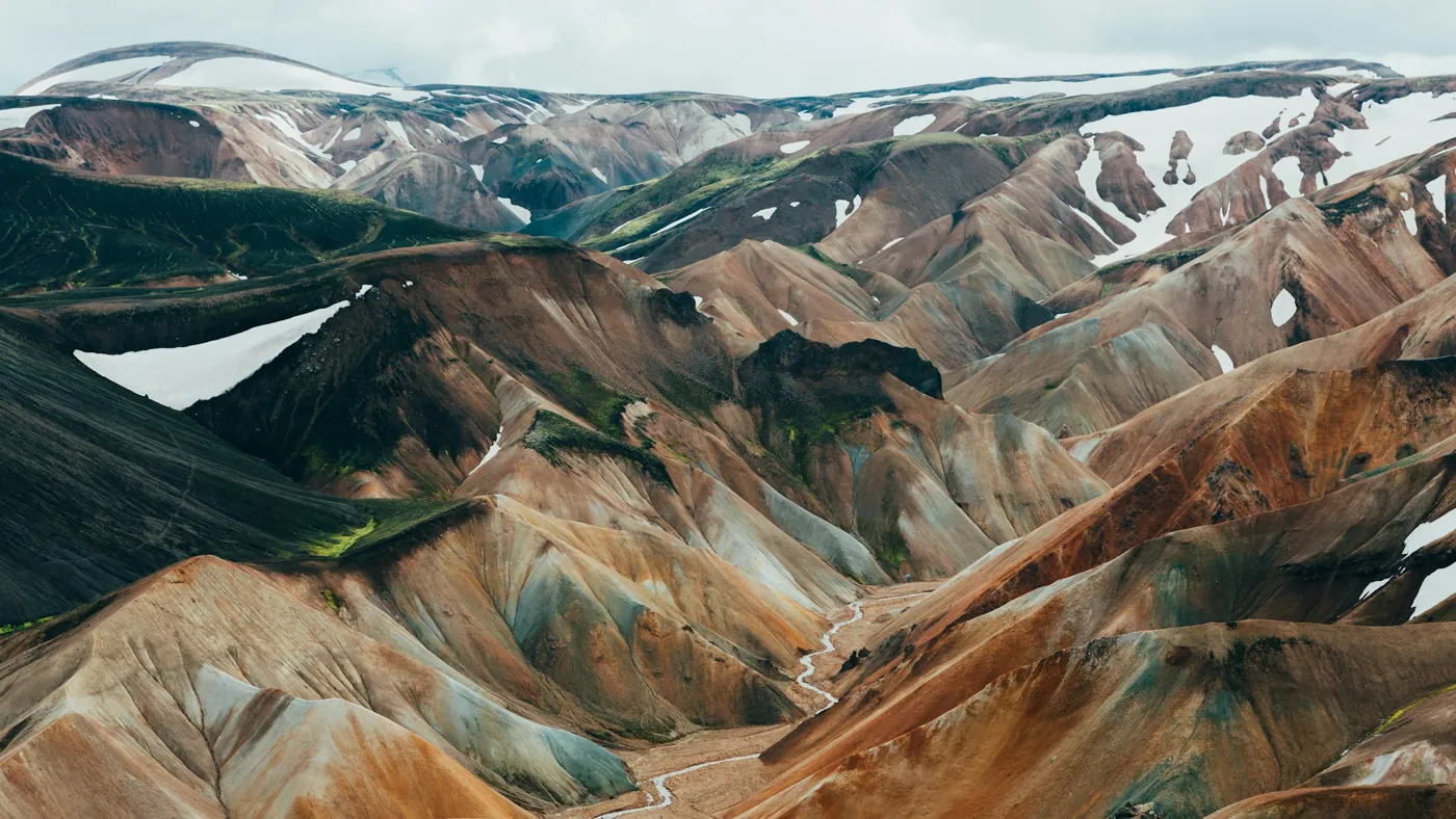 Bunte Rhyolithberge in Landmannalaugar mit Schneefeldern und einem Wanderweg im Tal