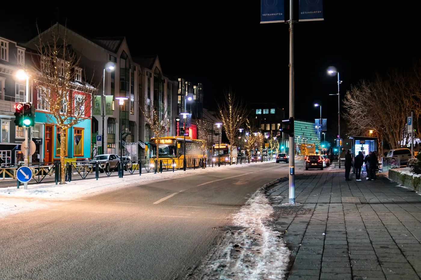 Beleuchtete Straße im Zentrum von Reykjavík bei Nacht mit Schneeresten am Gehweg
