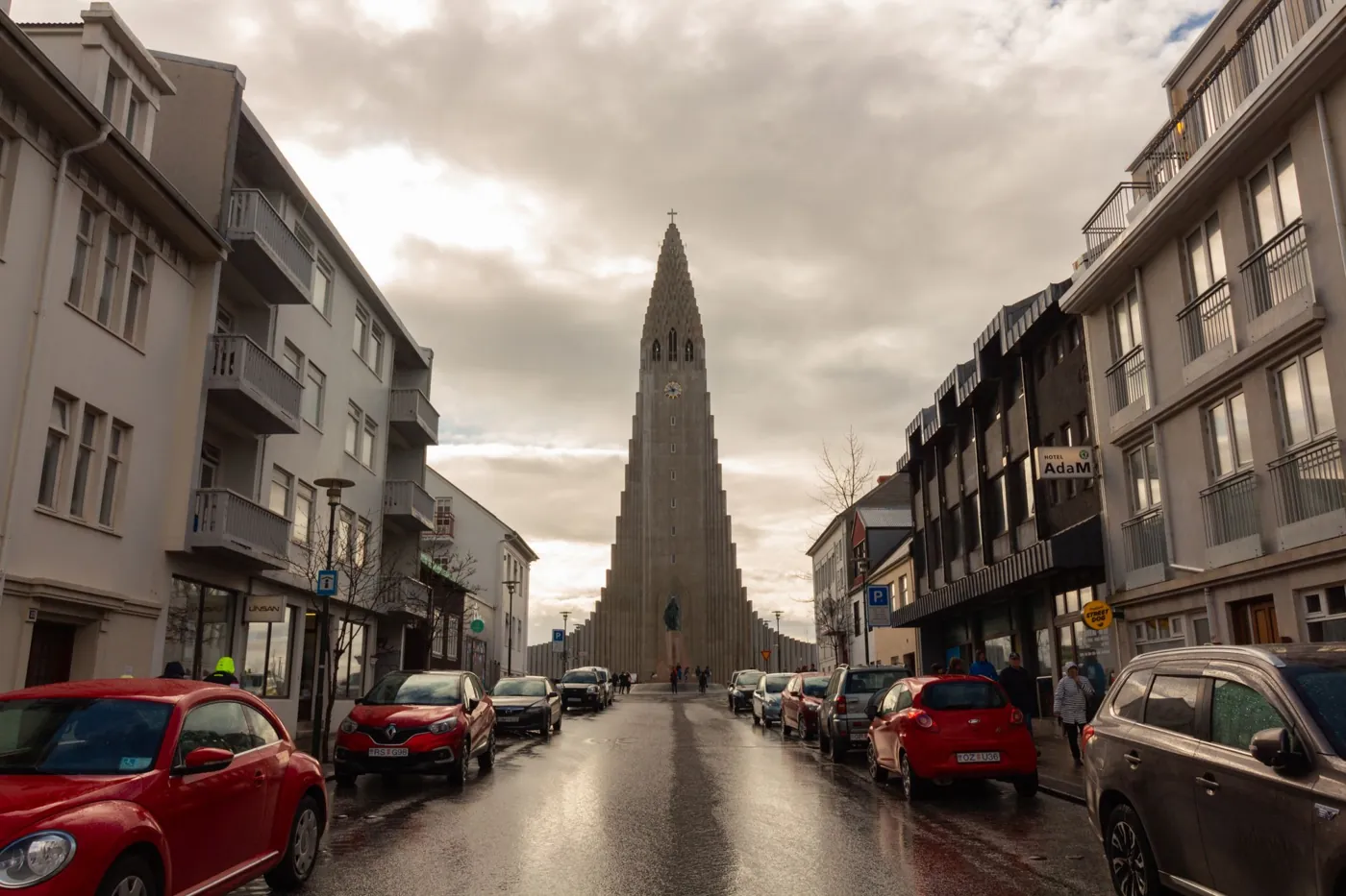 Regennasse Straße in Reykjavík mit parkenden Autos, am Ende die Hallgrímskirkja