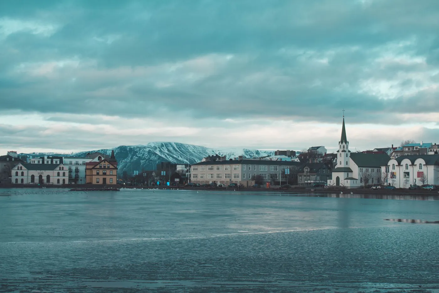 Reykjavík am Tjörnin-See im Winterlicht, dahinter schneebedeckte Berge
