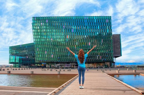 Frau steht mit ausgebreiteten Armen vor dem Harpa Konzerthaus in Reykjavik, Island