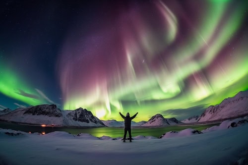 Person, die in einer schneebedeckten Landschaft mit den Nordlichtern am Himmel und einem See vor ihm steht