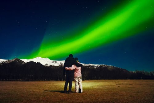 Paar beobachtet Nordlichter über schneebedeckten Hügeln Islands