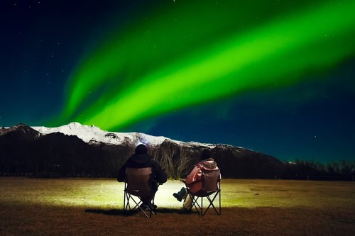 Paar in Campingstühlen sieht Nordlichter in Island
