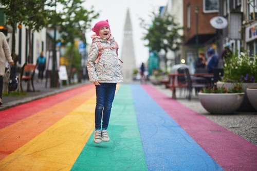Mädchen springt auf einer Regenbogenstraße in Reykjavik